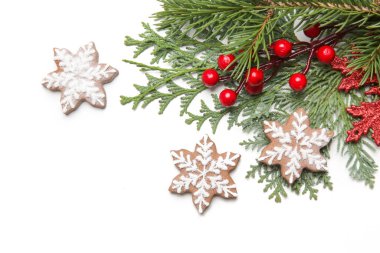 Noel süsü. Beyaz arka planda Noel ağacı dalları, kırmızı böğürtlen ve kar tanesi şeklinde kurabiyeler.