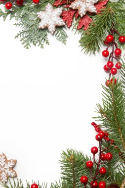 Noel süsü. Beyaz arka planda Noel ağacı dalları, kırmızı böğürtlen ve kar tanesi şeklinde kurabiyeler.