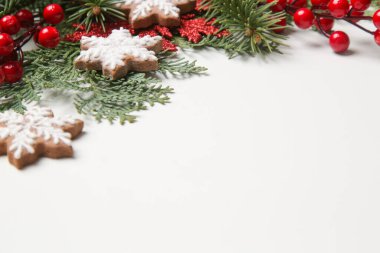 Noel süsü. Beyaz arka planda Noel ağacı dalları, kırmızı böğürtlen ve kar tanesi şeklinde kurabiyeler.