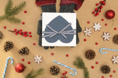 Yün eldivenli eller, Noel kemeri kutusunu köknar dalları, koniler, kurabiyeler ve süslemelerle birlikte masanın üzerinde tutuyorlar. Noel, kış tatili, yeni yıl konsepti.