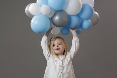 Bir grup beyaz ve mavi balon tutan mutlu küçük kızın stüdyo portresi. Kutlama, mutluluk, dilek ve umut kavramı.