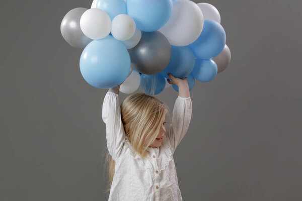 Studio portrait of happy little girl holding a group of white and blue balloons. Concept of celebration, happiness, wishes and hopes.