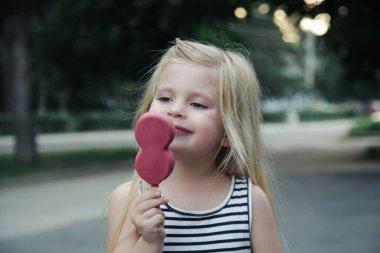 Küçük tatlı kız pembe buzlu şeker yiyor. Dondurmalı çocuk portresi..