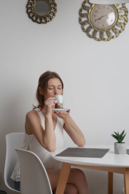 Genç bir kadın mutfak masasında oturuyor ve sabah kahvesinin tadını çıkarıyor.