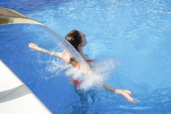 在游泳池瀑布射流下放松的年轻女子 — 图库照片
