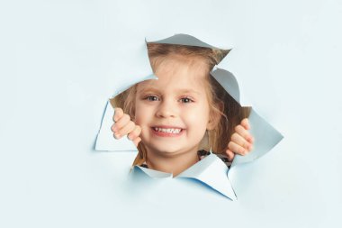 Sevimli küçük kız mavi yırtık kağıt delikten dikizliyor..