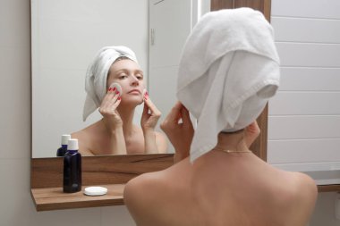 Güzel bir genç kadının portresi banyoda duruyor ve yüzünü aynanın önünde pamukla temizliyor, makyajı, güzelliği ve spa konseptini çıkarıyor..