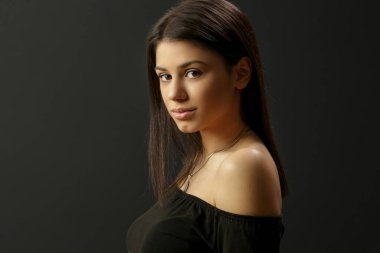 Siyah arka planda soğuk bir omuz giyen çekici genç esmer portresi.