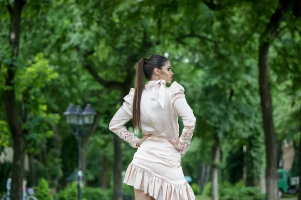 城市公园里穿着雅致缎子裙 留着长马尾辫的年轻貌美女子的户外肖像 — 图库照片