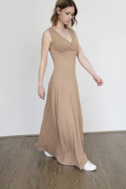 Uzun bej pamuklu elbiseli bir kadın. Rahat, asgari sükunetli moda tasarımı.
