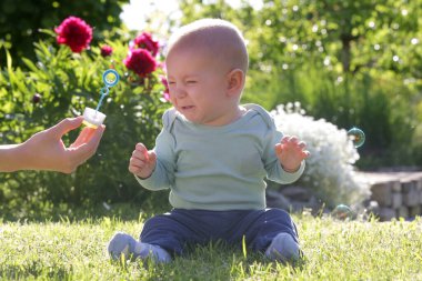 Güneşli yaz gününde bahçede sabun köpüğüyle oynayan tatlı bir erkek bebek. Mutlu çocukluk kavramı.