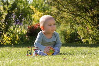 Çiçek bahçesinde oyuncaklarla oynayan sevimli mavi gözlü erkek bebek portresi.