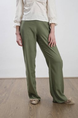 Kadın model keten elbise, beyaz bluz ve yeşil pantolon giyiyor. Stüdyo çekimi.