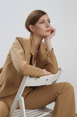 Bej takım elbiseli ve beyaz ipek bluzlu bir kadın model. Stüdyo çekimi.