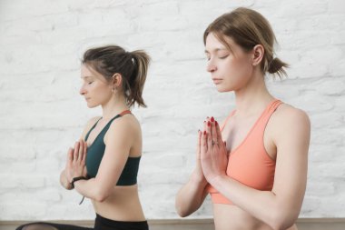 Yoga stüdyosunda meditasyon ve nefes egzersizi yapan iki genç kadın. Refah ve kendine bakım kavramı.