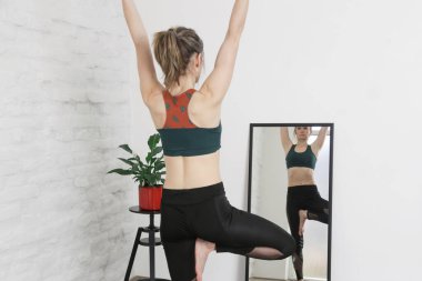 Stüdyoda yoga yapan genç bir kadın. Vrikshasana veya Ağaç Asana 'yı dengeleyen pozlar. 