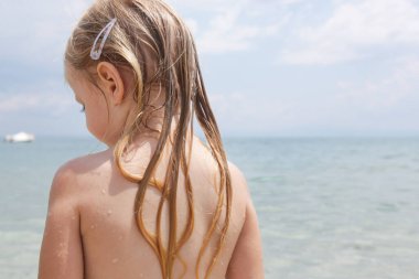 Çocuğun kumsaldaki uzun saçı. Islak saç, yakın plan görüntü. Tuzlu okyanus suyu ve güneşten kaynaklanan saç hasarı, yaz mevsimi saç bakımı konsepti.