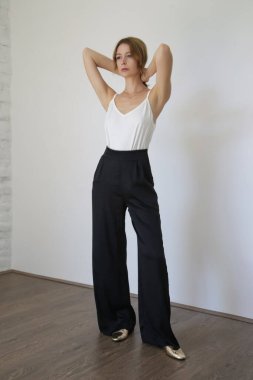 Beyaz pamuklu bluz ve siyah pantolon giyen bir kadın model. Klasik ve basit yaz modası. Stüdyo çekimi.