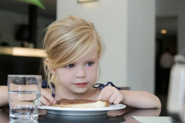 小さな女の子は朝食のためにパンのスライスにチョコレートクリームを食べる — ストック写真
