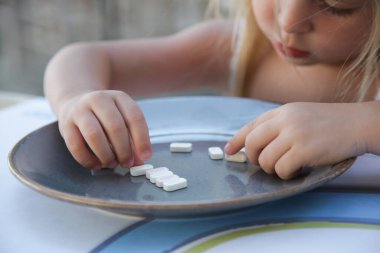 Yemek beklerken tabakta şekerlemelerle oynayan küçük kızın samimi portresi.