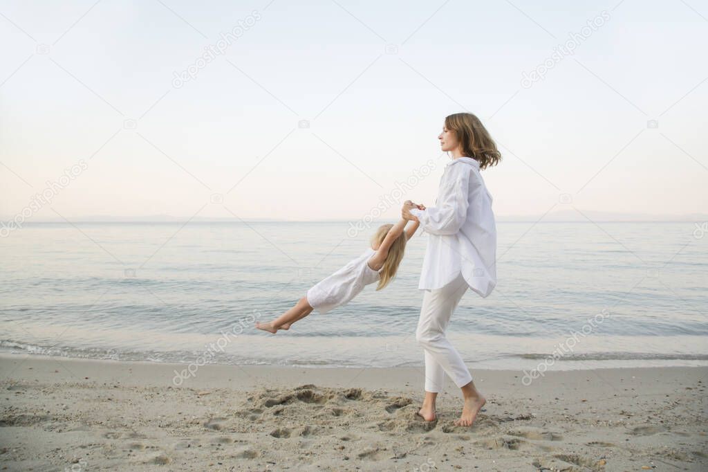 Mother and daughter having fun on the beach. Mother holding girls hands and spinning around. Family outdoor activities concept.
