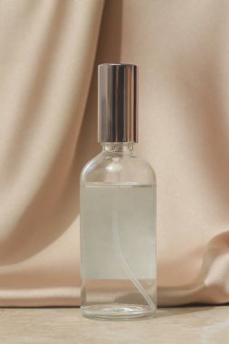 Yumuşak katlanmış ipek arka planda şeffaf sprey şişesi. Lüks kozmetik ve güzellik stili reklam kavramı.