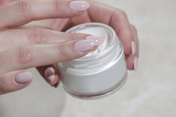 Close up of woman's hand is taking cream from a jar with her finger. Use of cosmetics with natural ingredients for clean and soft skin. Healthcare, skin care and beauty  concept.