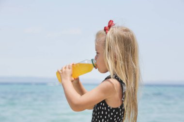 Little girl drinking electrolyte drink on the beach to avoid dehydration and heat illness on the summer vacation. Concept of keeping children hydrated and safe during a heatwave.
