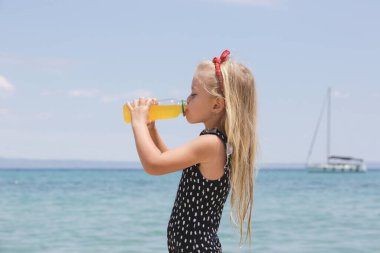 Little girl drinking electrolyte drink on the beach to avoid dehydration and heat illness on the summer vacation. Concept of keeping children hydrated and safe during a heatwave.