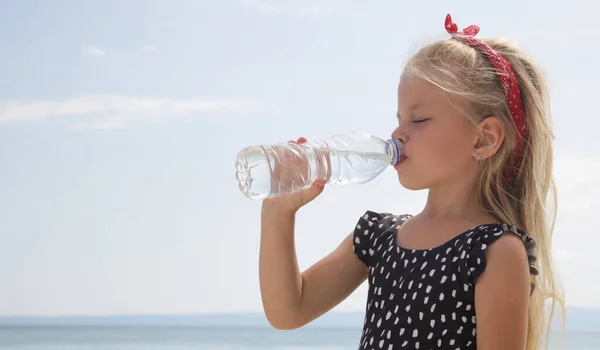 Little girl having water break on the beach to avoid dehydration and heat illness. Concept of keeping children hydrated and safe during a heatwave.