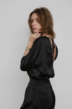 Serie of studio photos of young female model wearing all black classic basic outfit, silk satin blouse and wide legged trousers.