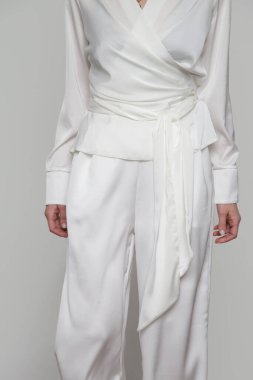 Serie of studio photos of young female model wearing all white classic outfit, silk satin wrap blouse and wide legged trousers.