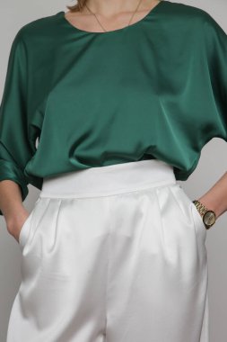 Serie of studio photos of young female model wearing emerald green silk satin batwing short sleeve blouse with white trousers.