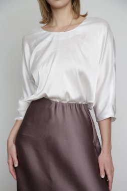 Series of studio photos of young female model wearing white silk satin batwing short sleeve blouse with mocha color midi skirt