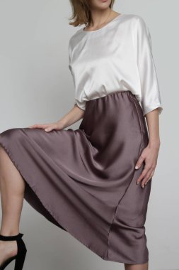 Series of studio photos of young female model wearing white silk satin batwing short sleeve blouse with mocha color midi skirt