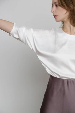 Series of studio photos of young female model wearing white silk satin batwing short sleeve blouse with mocha color midi skirt
