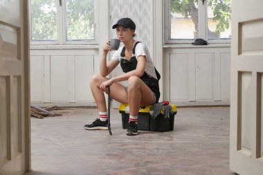 Young women resting during home renovation work, taking a coffee break during DIY home improvement project. 