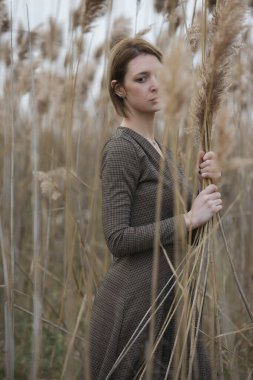Fashion outdoor portrait of young woman in autumn brown long sleeve dress.