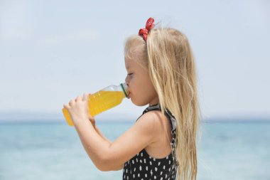 Little girl drinking electrolyte drink on the beach to avoid dehydration and heat illness on the summer vacation. Concept of keeping children hydrated and safe during a heatwave.