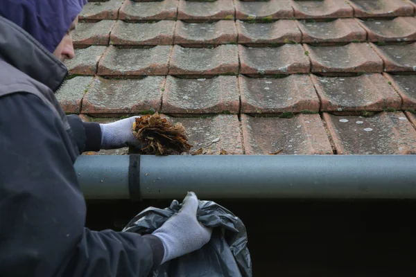Man cleaning the gutter from autumn leaves before winter season. Roof gutter cleaning process.
