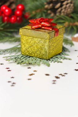 Kırmızı kurdeleli ve Noel süslemeli küçük altın bir hediye kutusu..