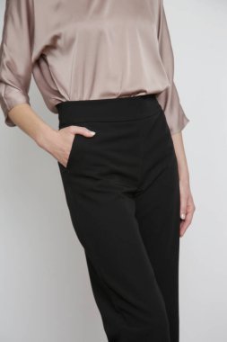 Stüdyo fotoğrafları. Siyah pantolonlu, ipek saten yarasa kanadı bluz giyen genç bir kadın model..