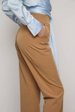 Stüdyo fotoğraflarında bej renkli, sıradan, sıradan pantolonlar giyen genç bir kadın model var.