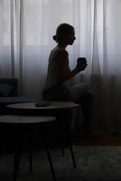 Woman drinking coffee next to the window