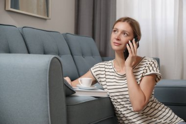 Rahatlamış genç bir kadın evde telefon, kahve ve kitapla dinleniyor.