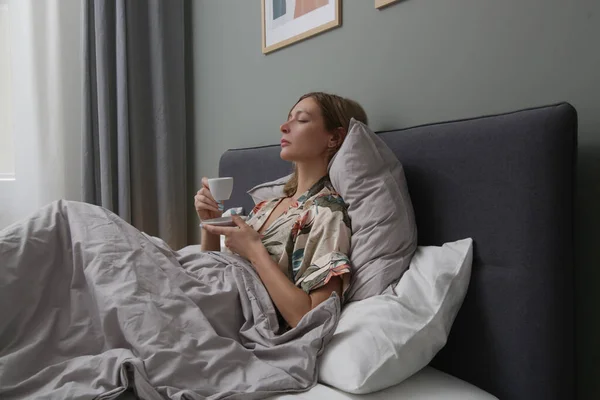 Serene woman drinking coffee in the bed, casual relaxing time alone
