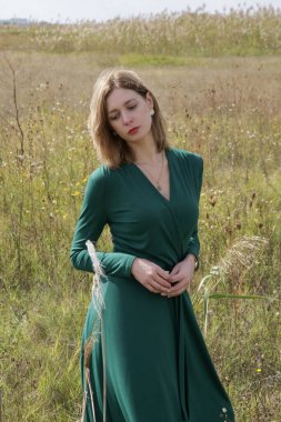 Yeşil elbiseli kadın modelin çayır üzerinde poz verdiği bir sürü fotoğraf. Doğal ışıklandırmalı açık hava portresi.
