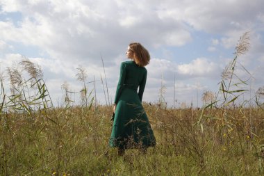 Yeşil elbiseli kadın modelin çayır üzerinde poz verdiği bir sürü fotoğraf. Doğal ışıklandırmalı açık hava portresi.