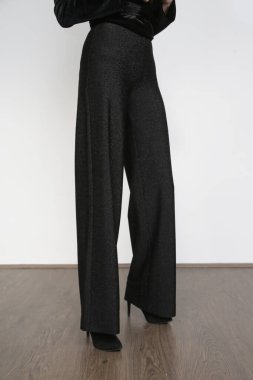 Stüdyo fotoğraflarında geniş siyah şık pantolonlar ve siyah topuklu ayakkabılar giyen kadın modeller var..