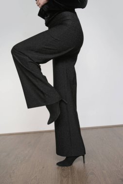 Stüdyo fotoğraflarında geniş siyah şık pantolonlar ve siyah topuklu ayakkabılar giyen kadın modeller var..